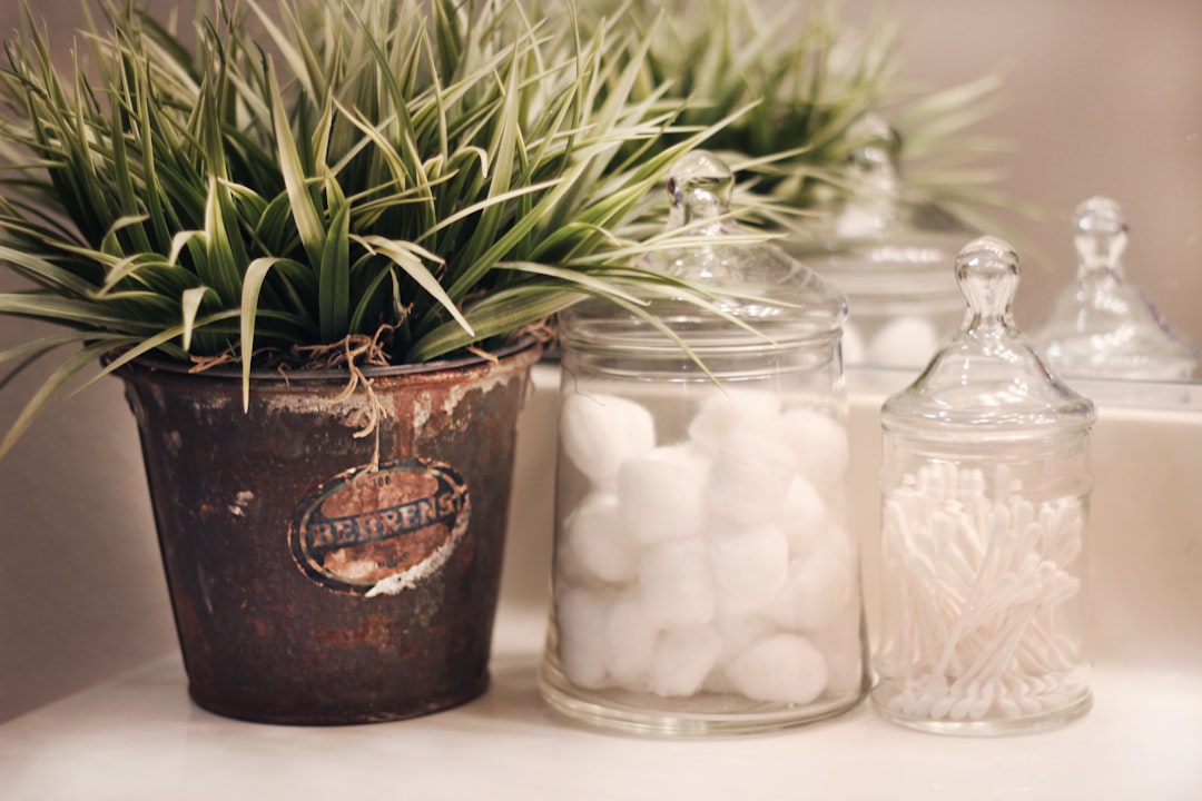 Vintage farmhouse decor on display in a bathroom, vintage advertising tin with faux green grass, apothecary jars with cotton balls and q-tips hold bathroom items in their pretty containers. An example of rustic, farmhouse home decor style.