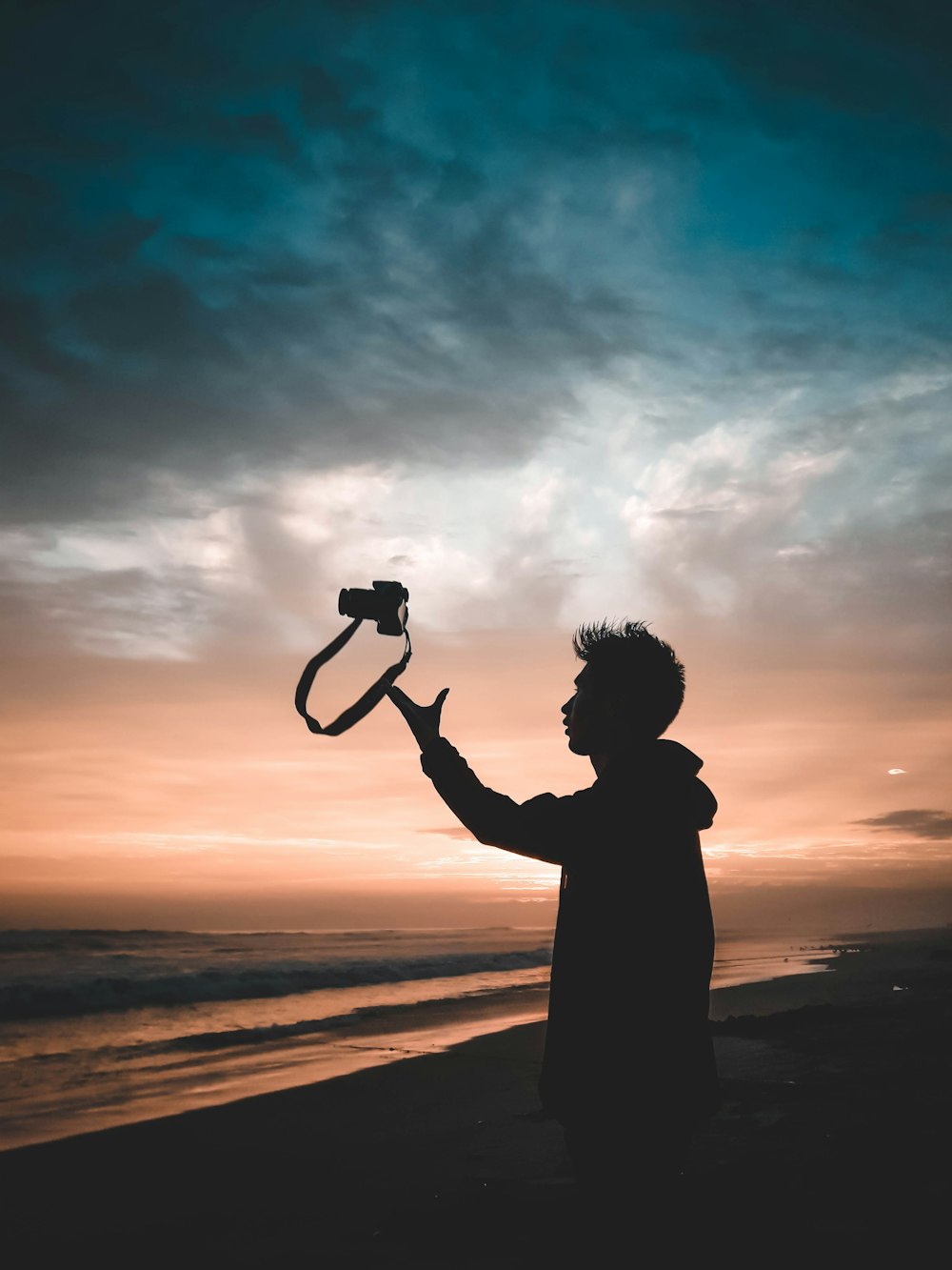 man throwing camera standing near shore during sunset