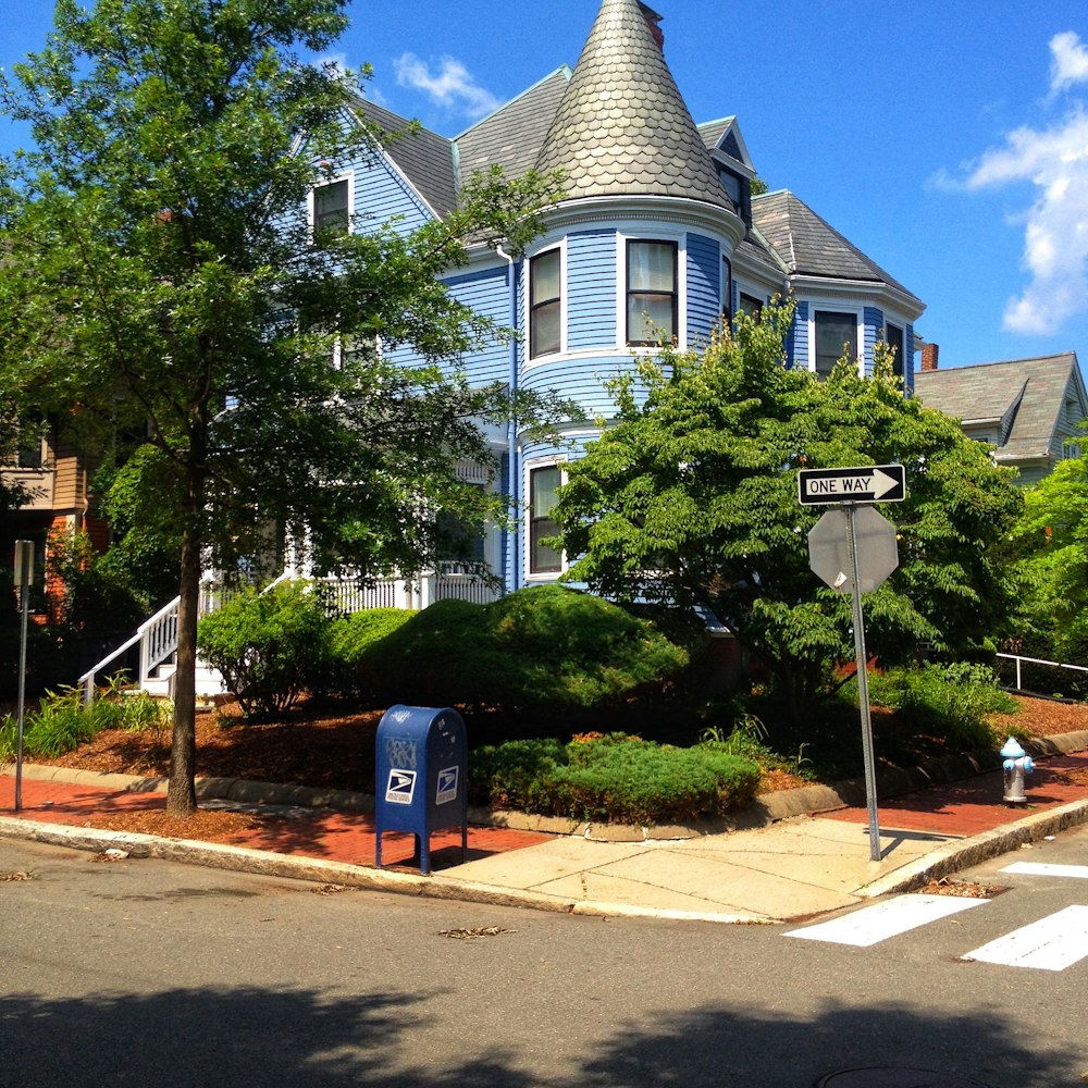 gray roofed blue 2-storey house covered by trees at the corner of street