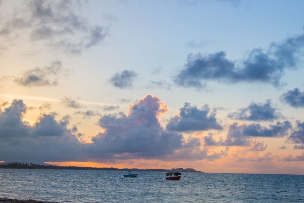 few boats on sea under blue and orange skies