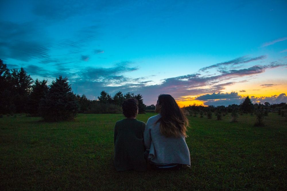 two women sitting on green grass field during blue hour