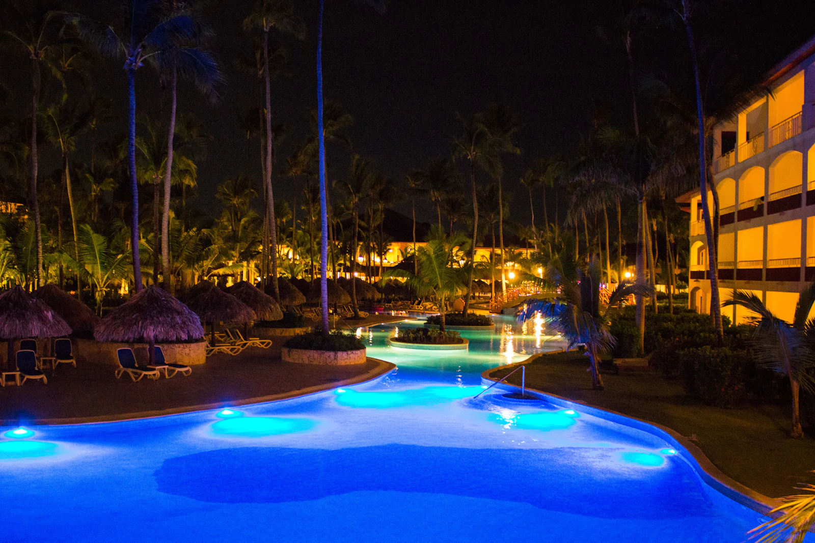 The main pool glowing at night, framed by palm trees and warm resort lights