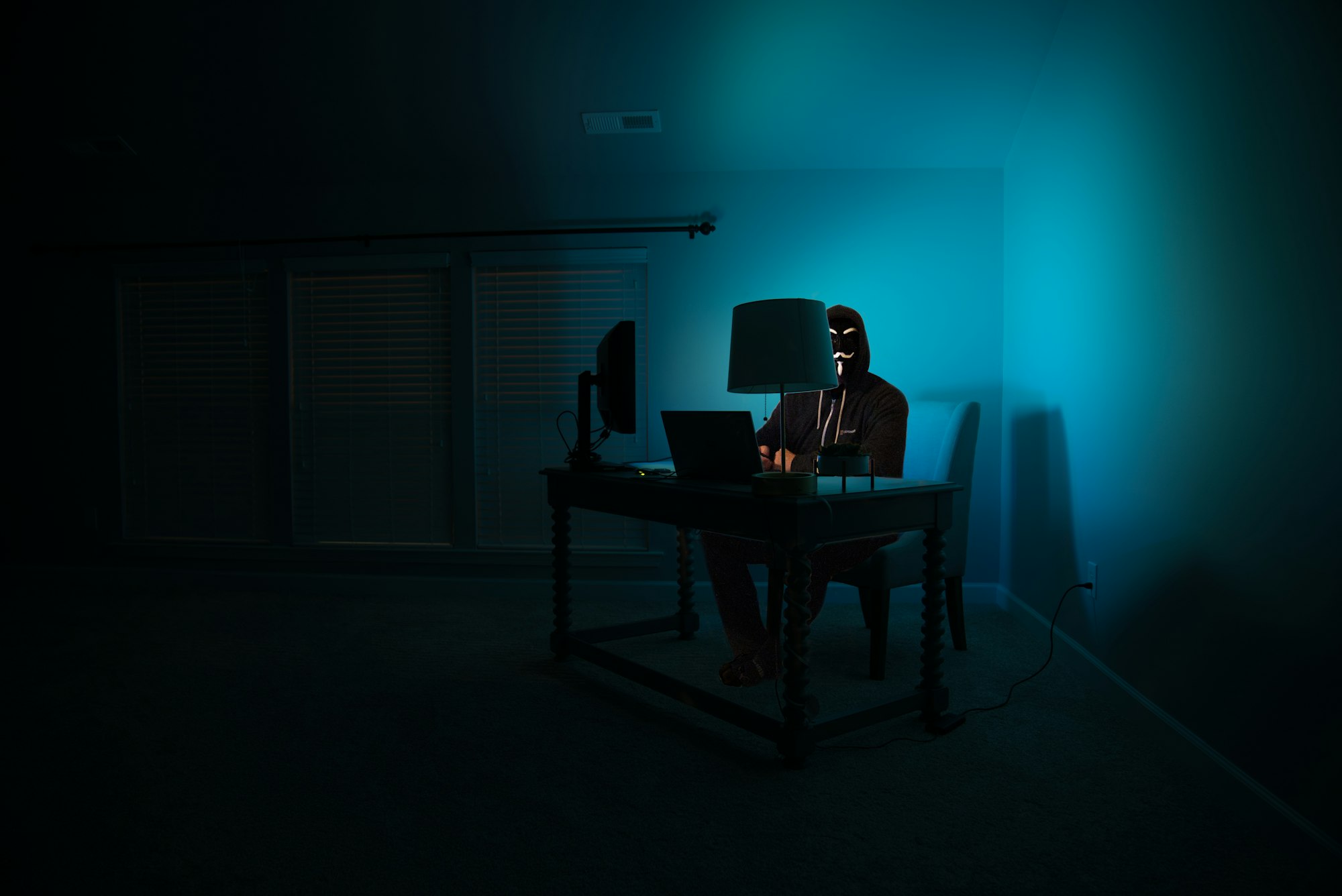 Pictured - a man at a computer disguised as an anonymous hacker wearing a Guy Fawkes mask.