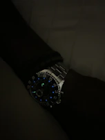 A wristwatch with a dark face and luminous hands glowing softly in low light.