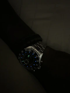 A wristwatch with a dark face and luminous hands glowing softly in low light.
