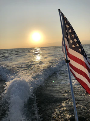 A coastal sunset with waves rolling in, silhouetted by a large American flag fluttering in the breeze.