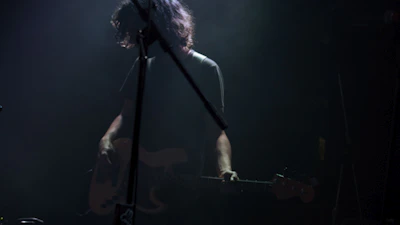Close-up of a musician performing live with a guitar under moody stage lighting.