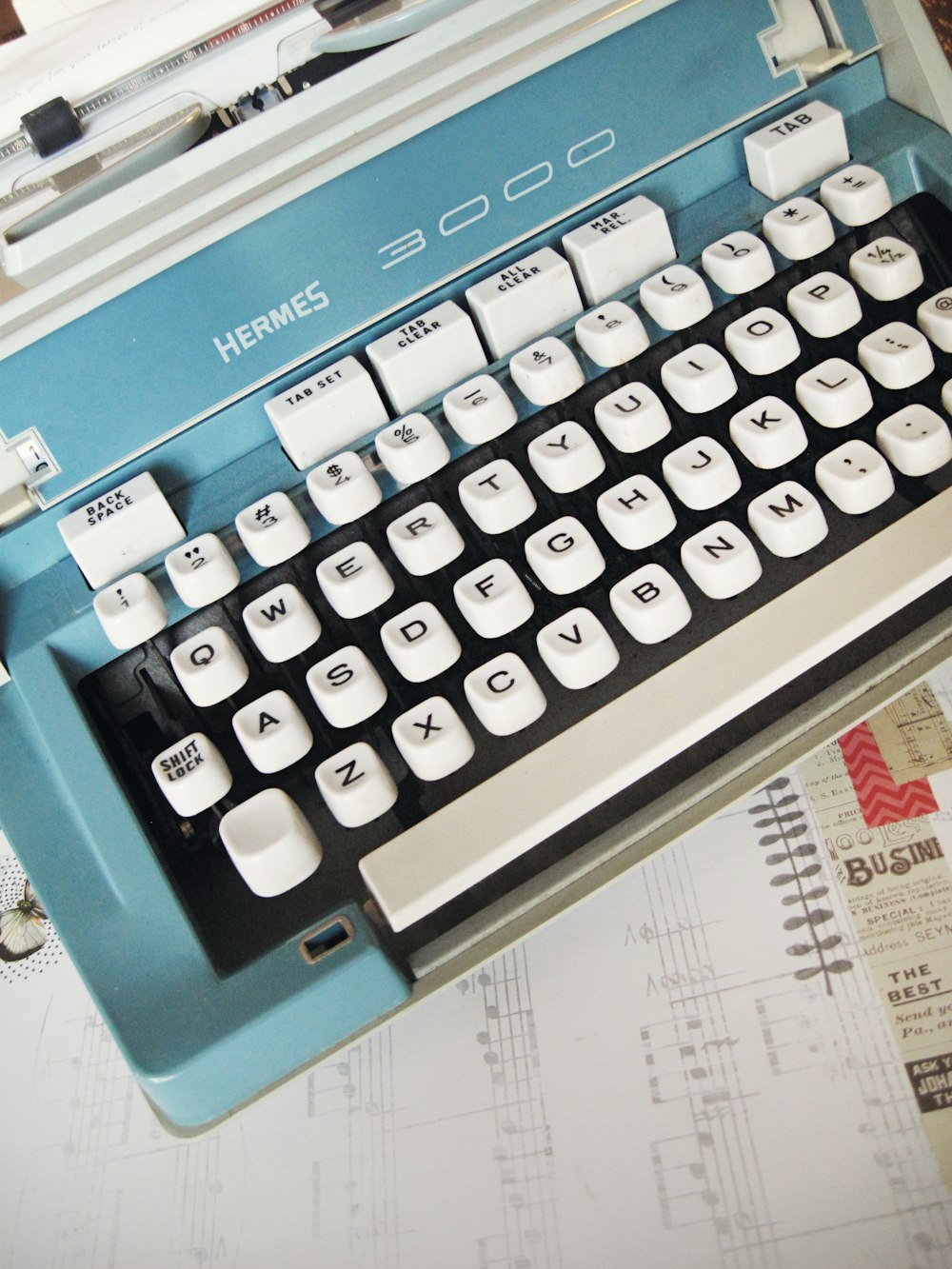 white and teal Hermes 3000 typewriter on white paper