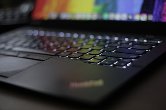Close-up view of a laptop keyboard with illuminated keys. The screen displays a colorful, blurred background. The angle highlights the sleek design and reflective surface of the keys.