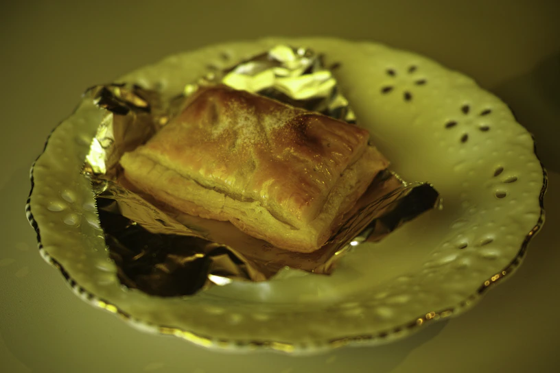 A beautifully plated golden pastry with delicate sugar dusting, set against a sleek black marble table.