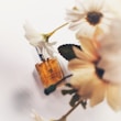 A perfume bottle labeled 'Moonlit Stroll' is lying on a light surface, partly surrounded by soft-focus white flowers. The bottle is predominantly golden in color, evoking a sense of elegance and warmth.