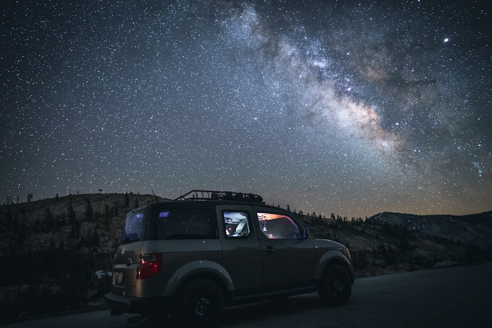 grey SUV parked on side of road under starry night sky