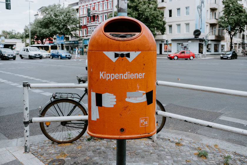 An orange metal street collection container standing on a paved kerbside.