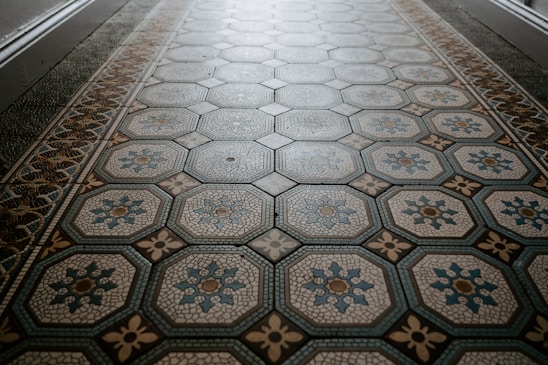 An ornate tiled floor with a hexagonal pattern, featuring intricate designs in shades of blue and beige. The central motif of each tile includes floral elements outlined in different colors.