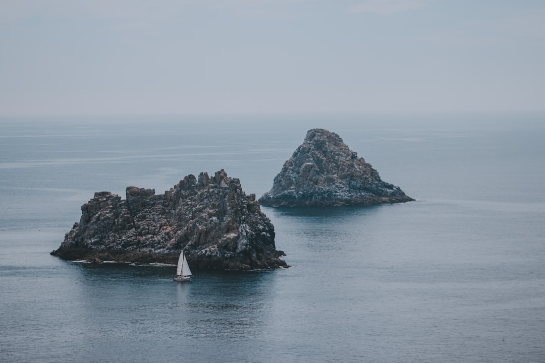 white sailboat passing grey rock island in sea