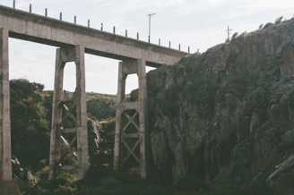 A sturdy concrete bridge spanning a river valley surrounded by mountainous landscape.