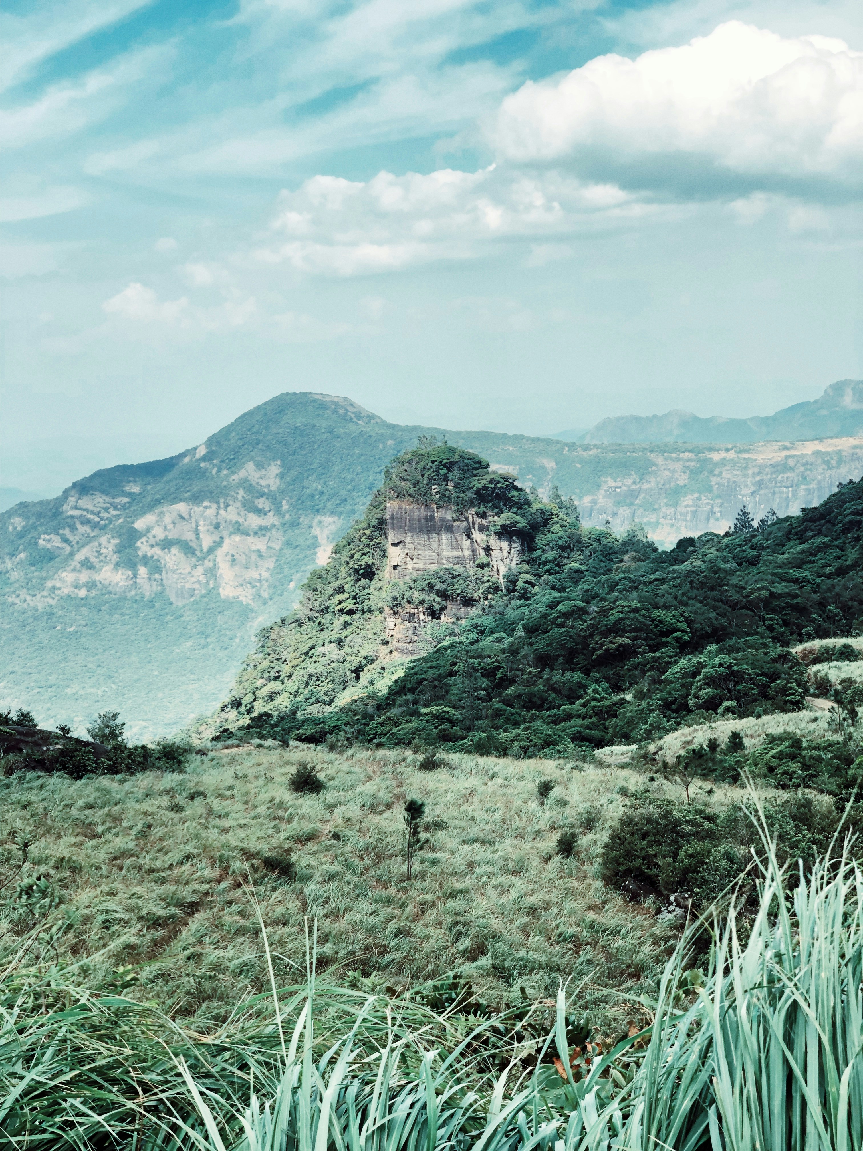 mountain and green field under blue and white skies