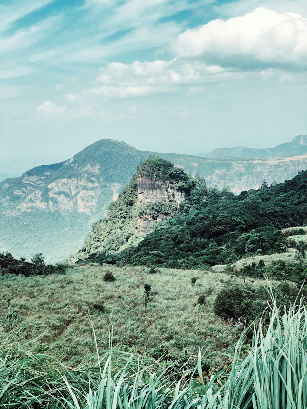 mountain and green field under blue and white skies