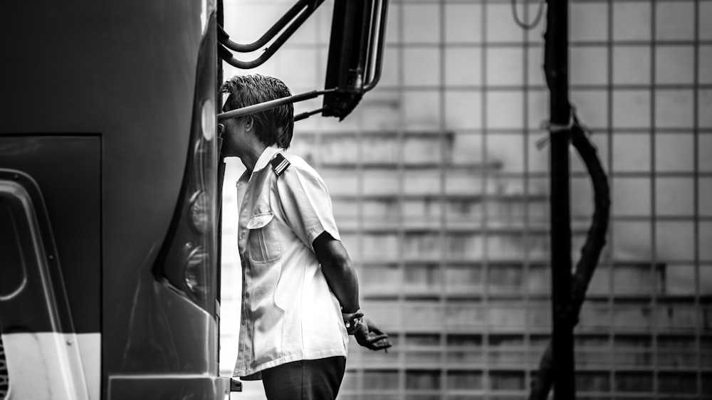 grayscale photography of man standing beside bus