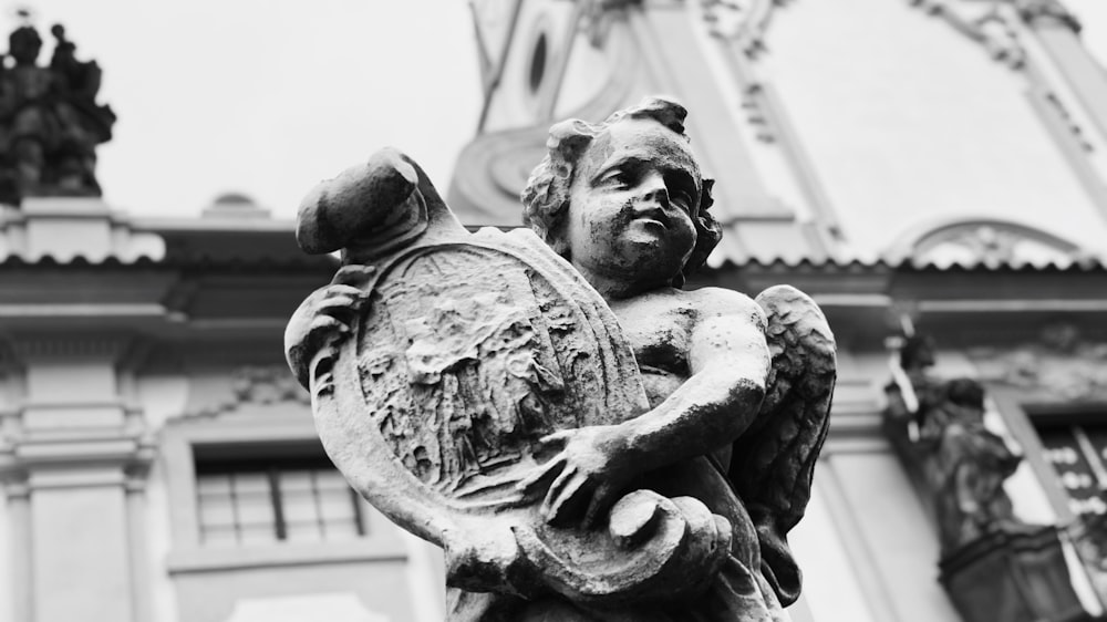 grayscale photography of cherub playing harp statue