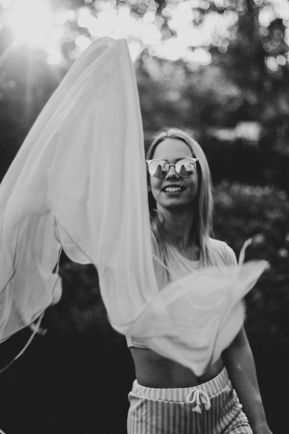 grayscale photography of smiling woman trowing textile near outdoor during daytime