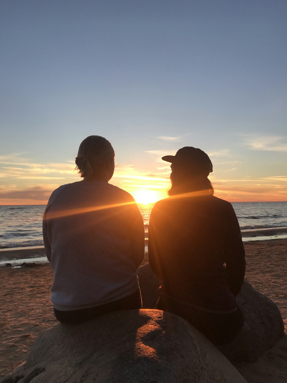 two person sitting on rock facing on sea