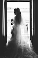 An elegant portrait of a bride looking out a window, light casting gentle shadows.