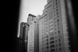 A black and white photograph capturing a cluster of tall, residential buildings. The structures are modern, with numerous windows arranged in a grid pattern. The angle of the photo gives a sense of height and urban density.