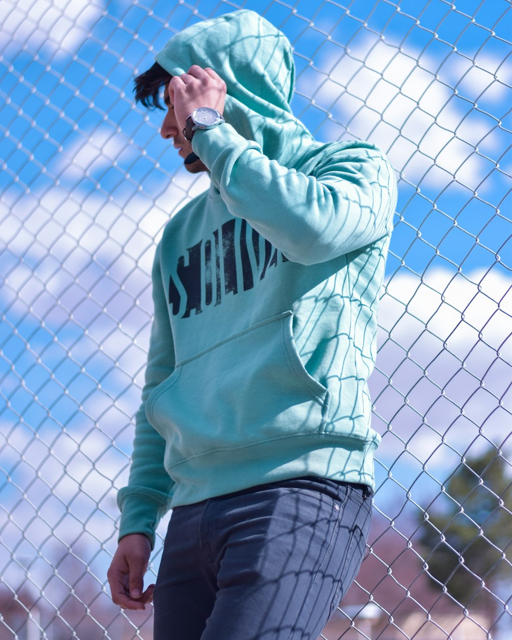 man leaning behind chain-link fence during daytime