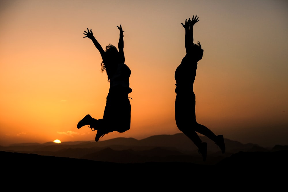 Silueta de dos personas que saltan durante la puesta del sol