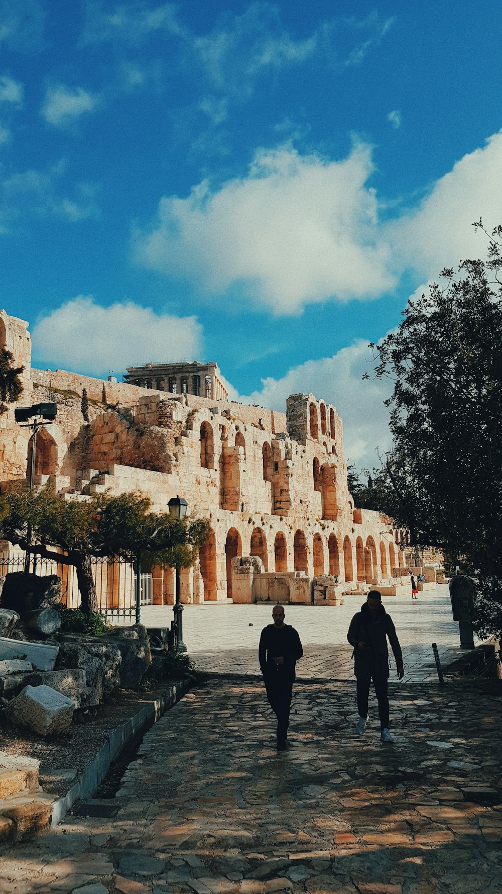 two people walking near ruins under white and blue cloudy sky