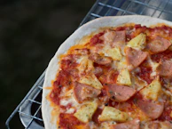 A rustic pizza with ham, pineapple, and melted cheese on a dark background