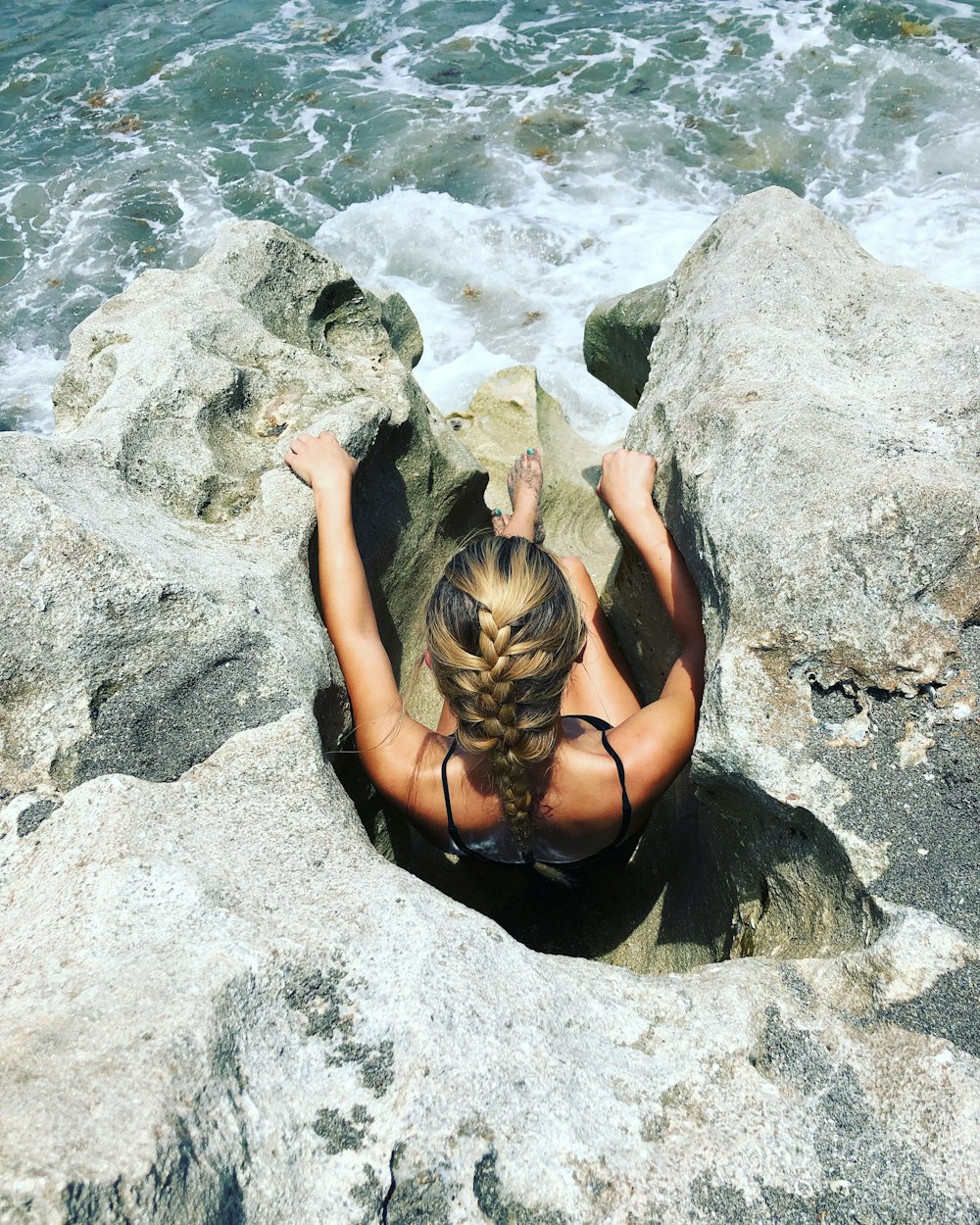 woman sitting in between rock gaps above the sea