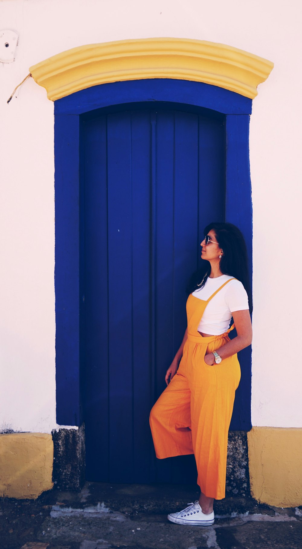 woman wearing yellow orange overalls leaning near blue painted door