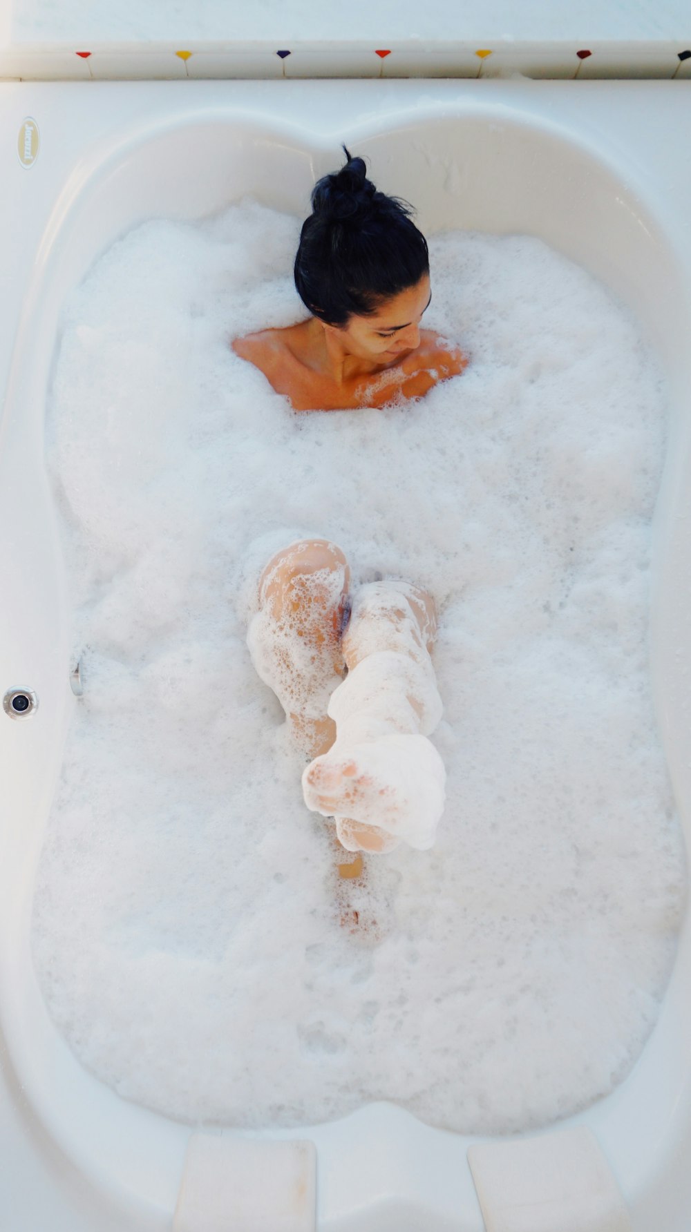 Fotografie einer Frau in der Badewanne, die mit weißen Seifenblasen bedeckt ist