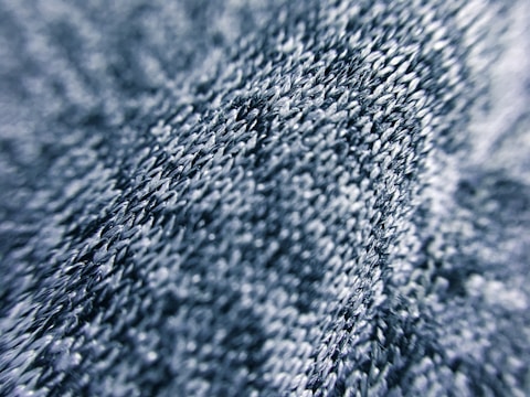 Close-up view of a textured fabric surface with intricate stitching and a wavy pattern. The threads appear in various shades of blue, giving depth and dimension.