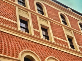 A brick facade of a building with multiple windows framed in a cream-colored trim. The brickwork is detailed and uniform, and the windows are evenly spaced with arch designs above them.
