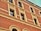 A brick facade of a building with multiple windows framed in a cream-colored trim. The brickwork is detailed and uniform, and the windows are evenly spaced with arch designs above them.