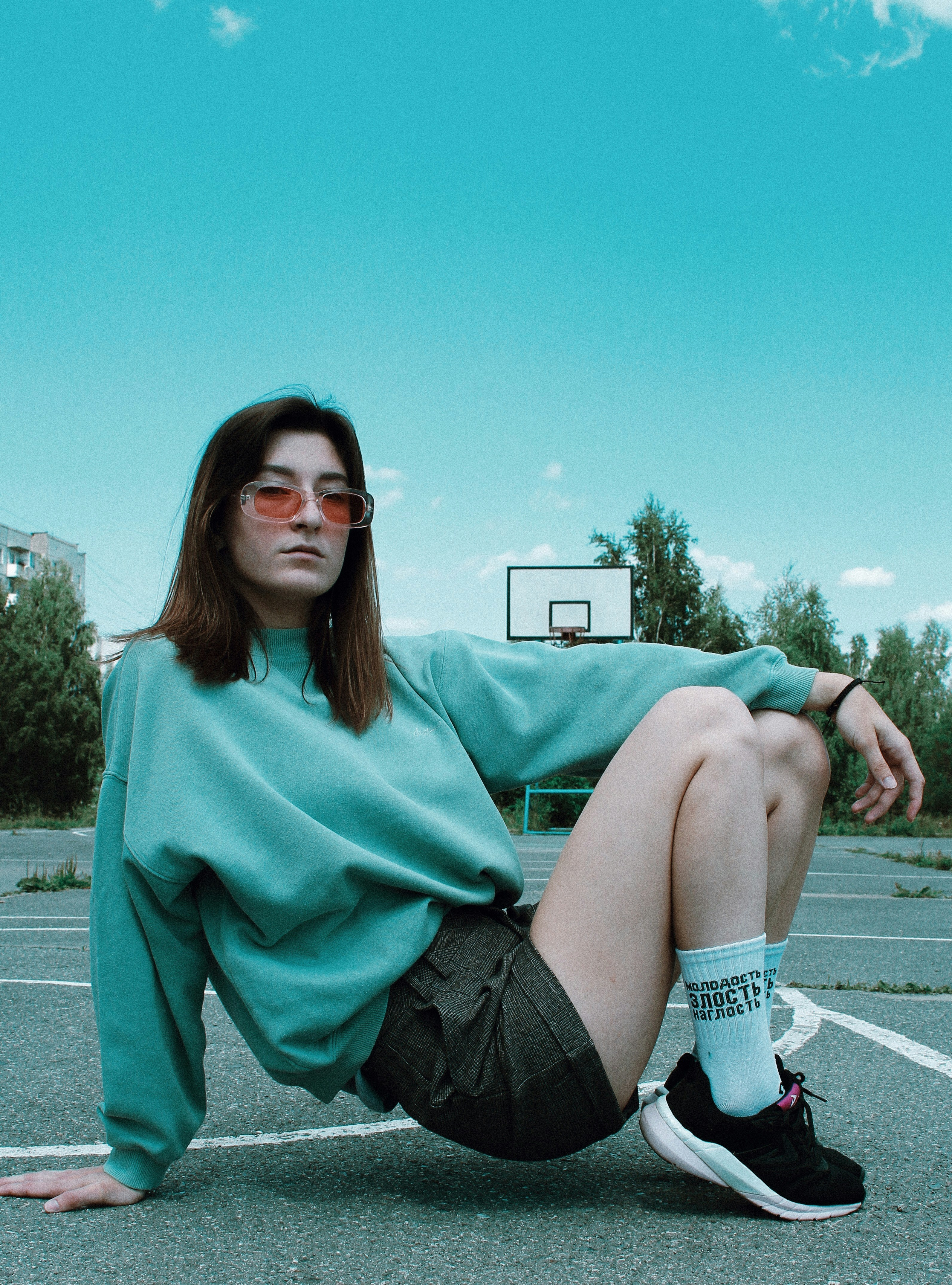 Wanita dengan sweater dan celana pendek hendak duduk di lapangan basket di bawah langit biru cerah