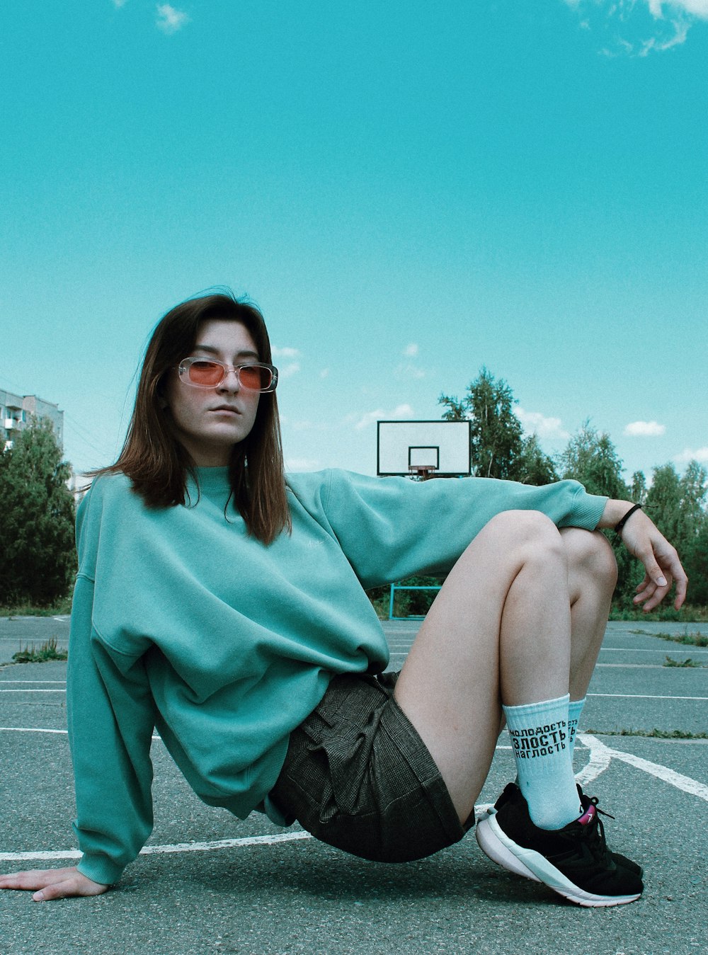 woman in sweater and shorts about to sit on basketball court under clear blue sky