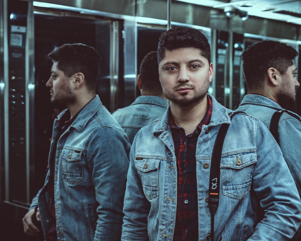 man wearing blue denim jacket standing beside mirror