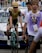 A cyclist wearing a yellow and black racing outfit with a matching helmet is riding a Bianchi bike, followed by people who appear to be in a race setting. Behind them, a white support vehicle with a rooftop rack is visible, and a person wearing a purple vest marked 'DEPART 70' walks nearby.
