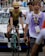 A cyclist wearing a yellow and black racing outfit with a matching helmet is riding a Bianchi bike, followed by people who appear to be in a race setting. Behind them, a white support vehicle with a rooftop rack is visible, and a person wearing a purple vest marked 'DEPART 70' walks nearby.