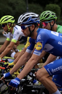 Several cyclists are intensely focused as they ride closely together during a race. The cyclists are wearing colorful jerseys and helmets, indicating a professional competition environment.