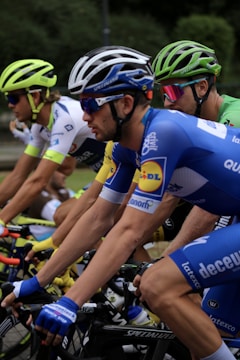 Several cyclists are intensely focused as they ride closely together during a race. The cyclists are wearing colorful jerseys and helmets, indicating a professional competition environment.