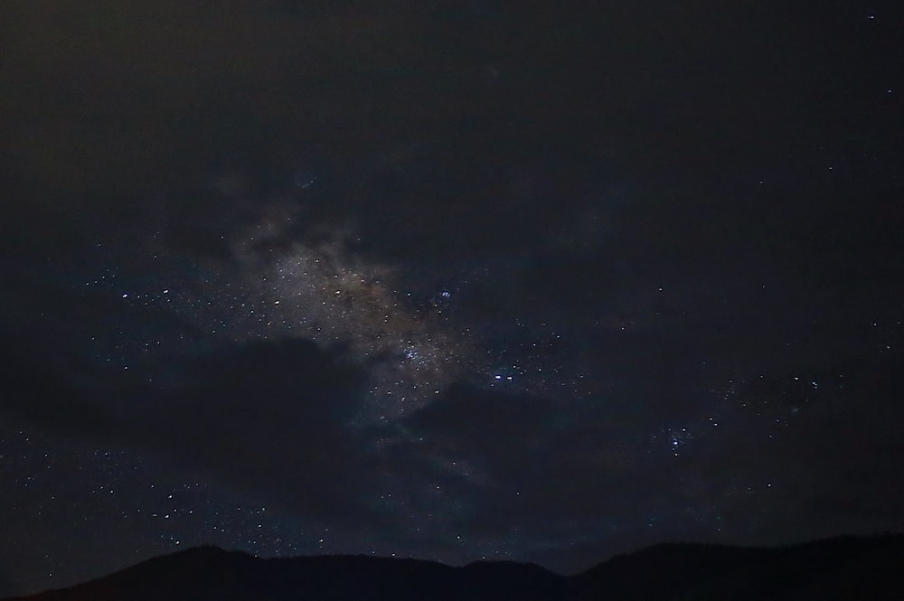 the night sky with stars and clouds above mountains