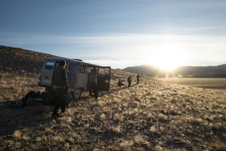 A rugged van parked beside a winding mountain road at golden hour, with a lone male traveler setting up camp.