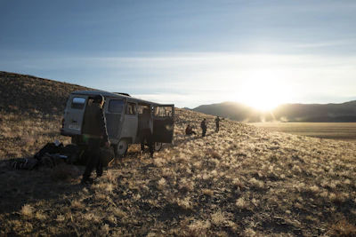 A rugged mountain scene with a man preparing his van for a journey at dawn.