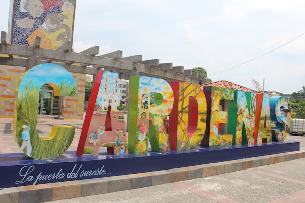 Large colorful letters spelling 'Cardenas' are displayed in a public area, each letter painted with vibrant, detailed scenes depicting various aspects of culture, nature, and daily life. The base of the display features the phrase 'La puerta del sureste...' in elegant script.