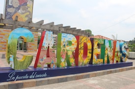 Large colorful letters spelling 'Cardenas' are displayed in a public area, each letter painted with vibrant, detailed scenes depicting various aspects of culture, nature, and daily life. The base of the display features the phrase 'La puerta del sureste...' in elegant script.